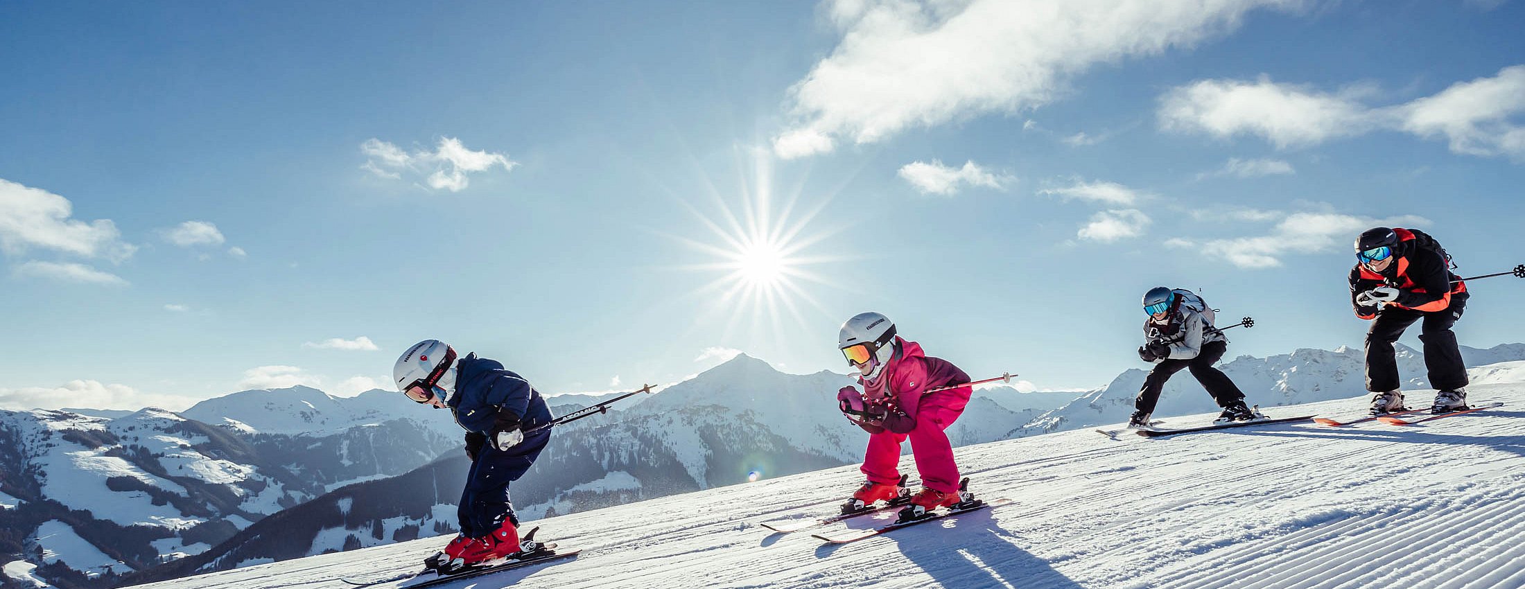 Kinder fahren in Reihe bei strahlendem Sonnenschein über eine präparierte Skipiste