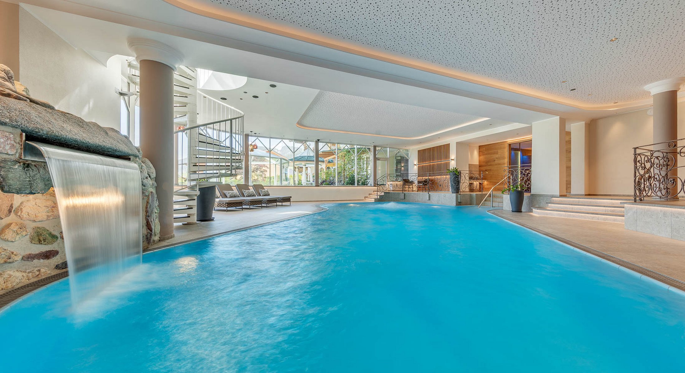 Erhöhte Ruhegalerie mit komfortablen Wellnessliegen und stilvollem Holzdesign am Hotel-Pool
