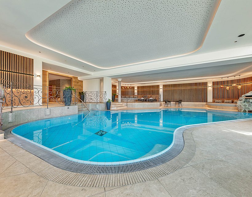 Lichtdurchflutetes Hallenbad im Hotel-Wellnessbereich mit geschwungenem Pool und Ruheliegen